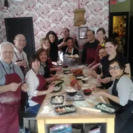Group cooking class with smiling participants around a table making food.