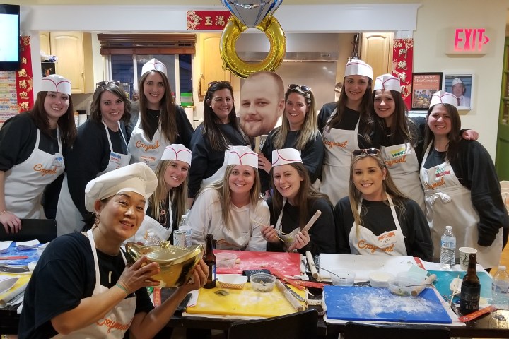 Group of smiling people in chef hats and aprons posing in a kitchen setting with cooking tools.