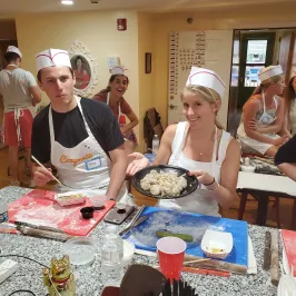 People in chef hats at a cooking class, one holding a plate of dumplings.