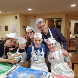 Group of people in chef hats and aprons posing happily in a kitchen setting.
