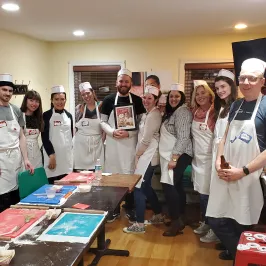Group of people in aprons and hats posing in a cooking class setting.