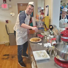 Person in apron and hat making food in a kitchen, with dumplings and a mixer on the table.