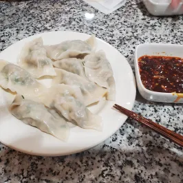 Plate of dumplings with soy sauce in a small dish and chopsticks on a granite countertop.