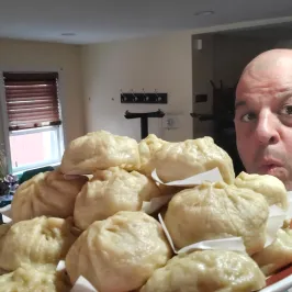 Person posing with a plate of stacked steamed buns in a room with a window and poster.