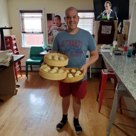 Person holding trays of steamed buns in a living room with a TV showing a movie.