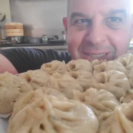 Person smiling with a plate of dumplings in a kitchen setting.