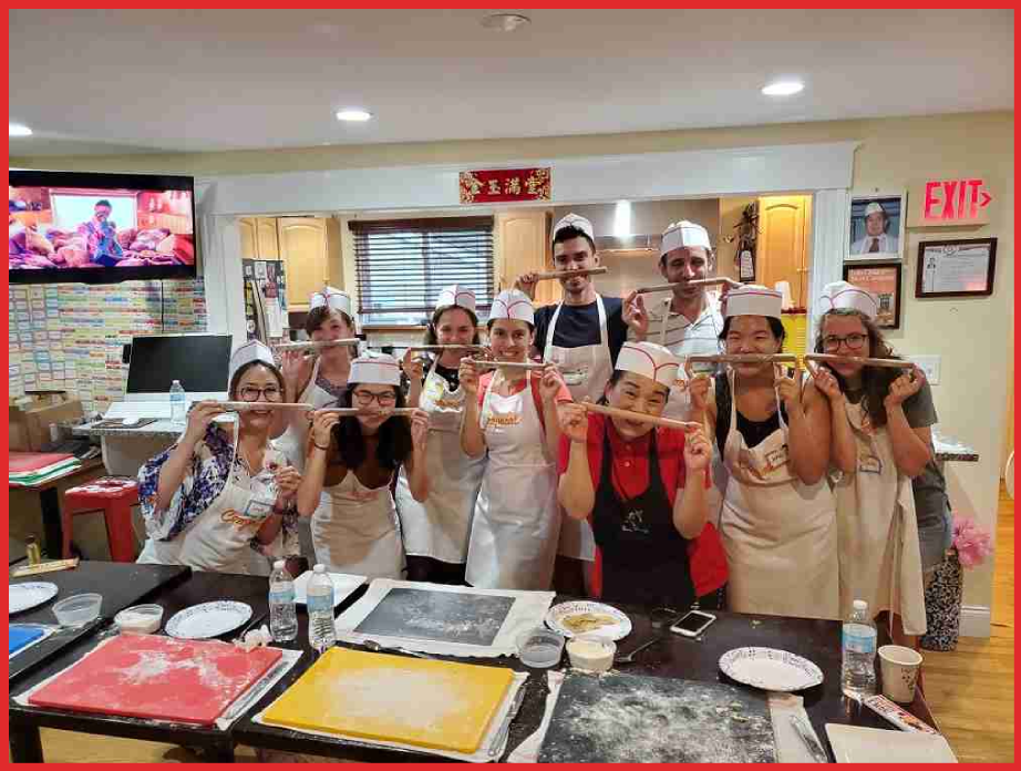 Dumpling Party Group photo of people in aprons holding dough in a kitchen setting.