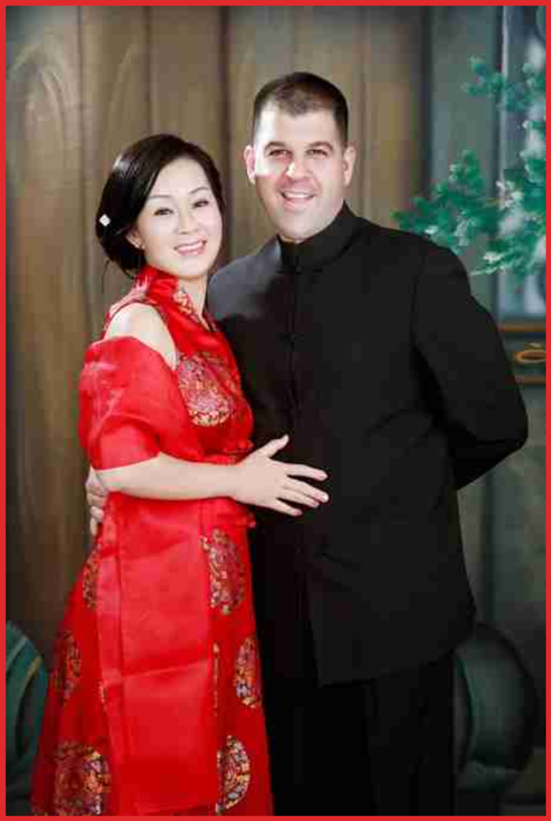 Patty Chen Smiling couple in formal attire, woman in red dress, man in black suit, standing indoors.