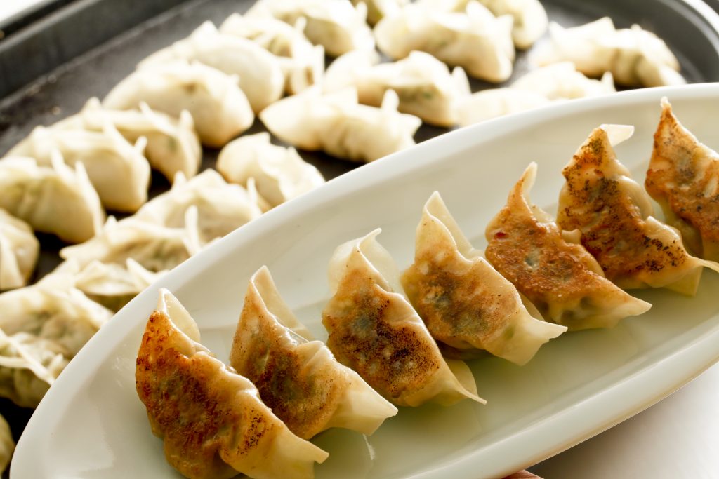Close-up of pan-fried dumplings on a white plate with more dumplings in the background.