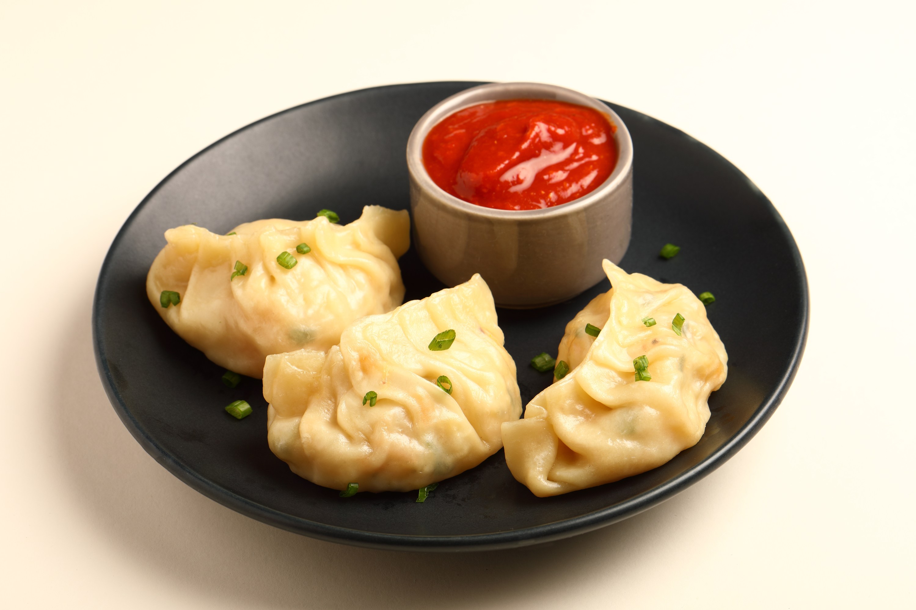 Three dumplings on a black plate with red sauce.